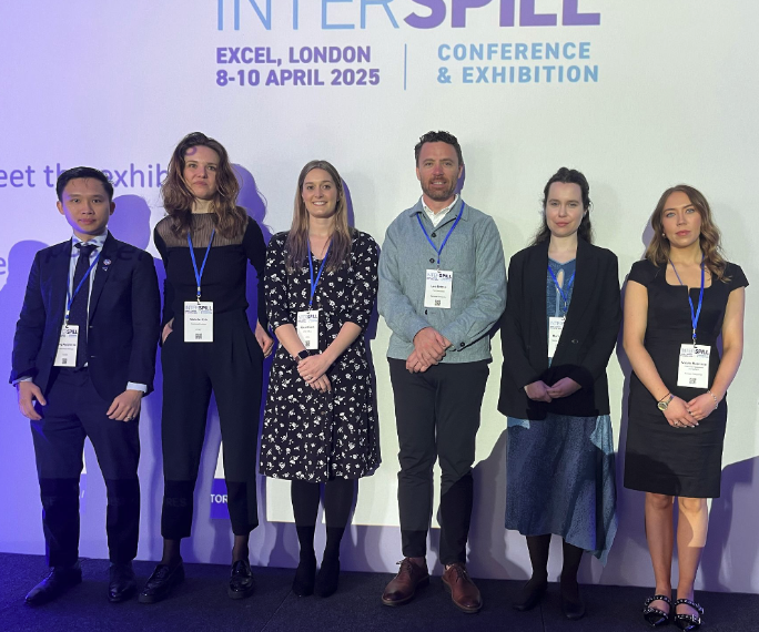 Six smiling attendees pose in front of an InterSpill 2025 banner, capturing a moment of camaraderie and professionalism.